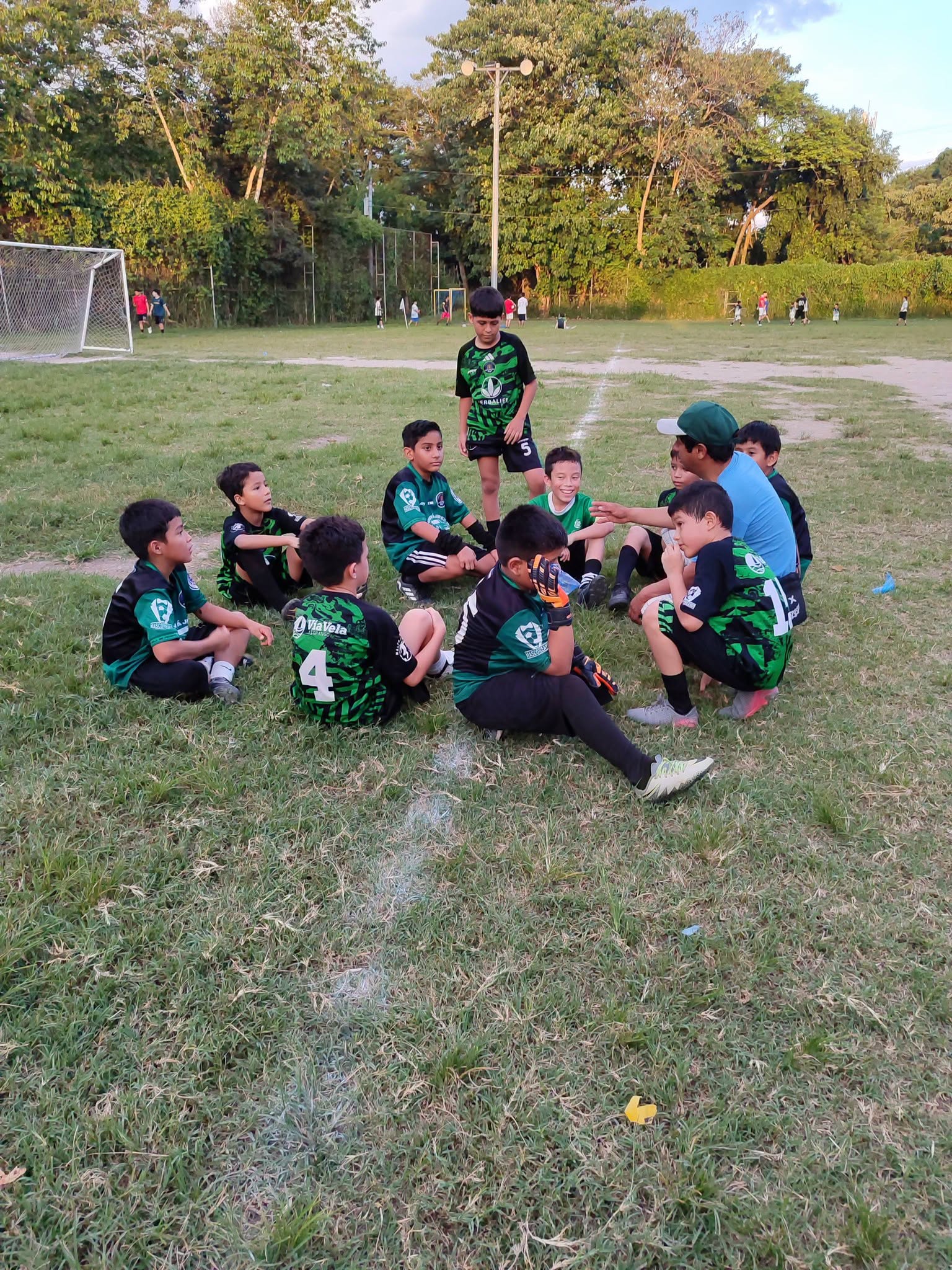 Entrenador conversando con niños del equipo sentados en la cancha
