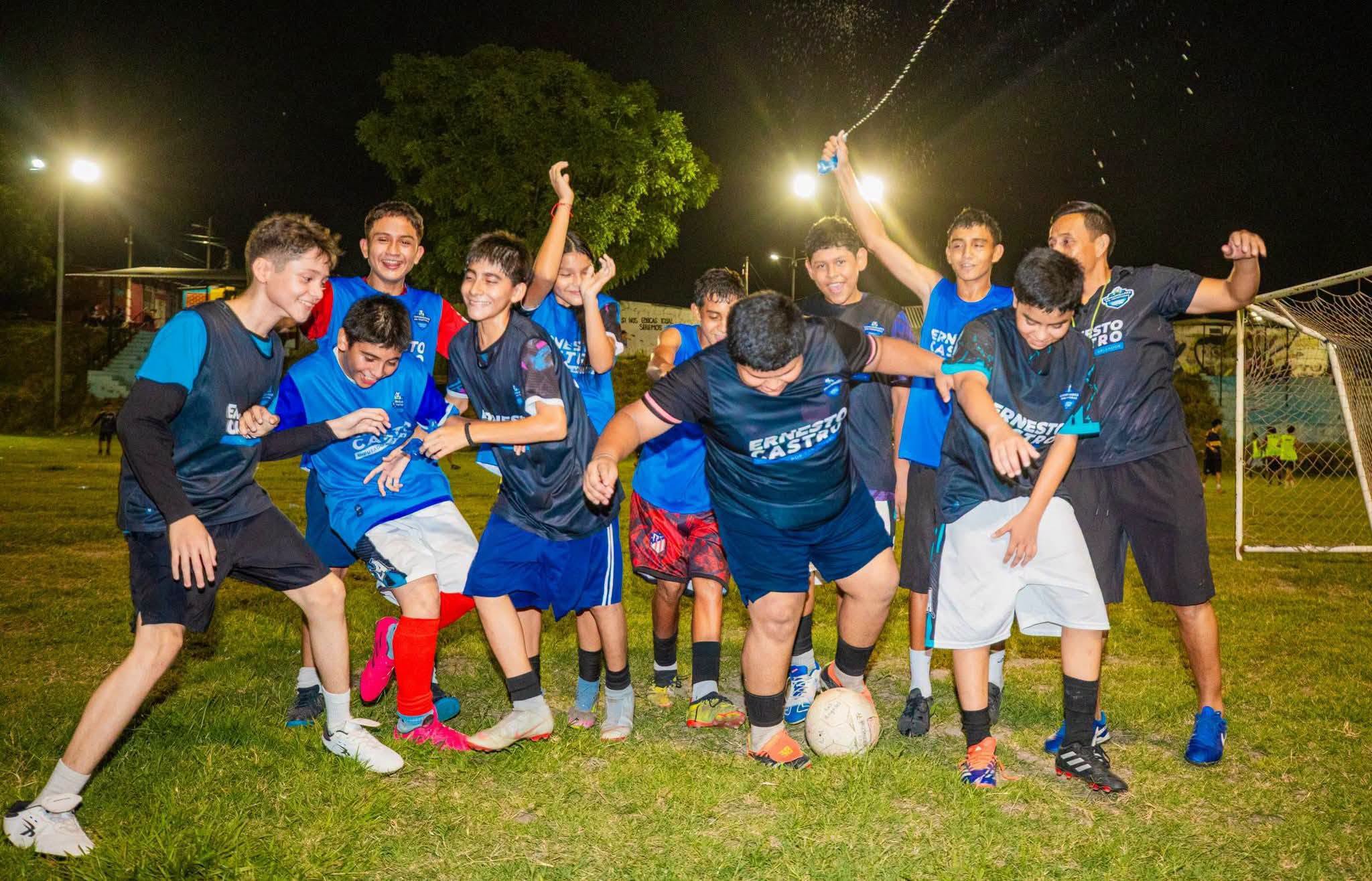 Niños celebrando juntos con el balón en una cancha de noche